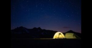 星空の下でキャンプをしていて、テントに明かりが点いている風景写真